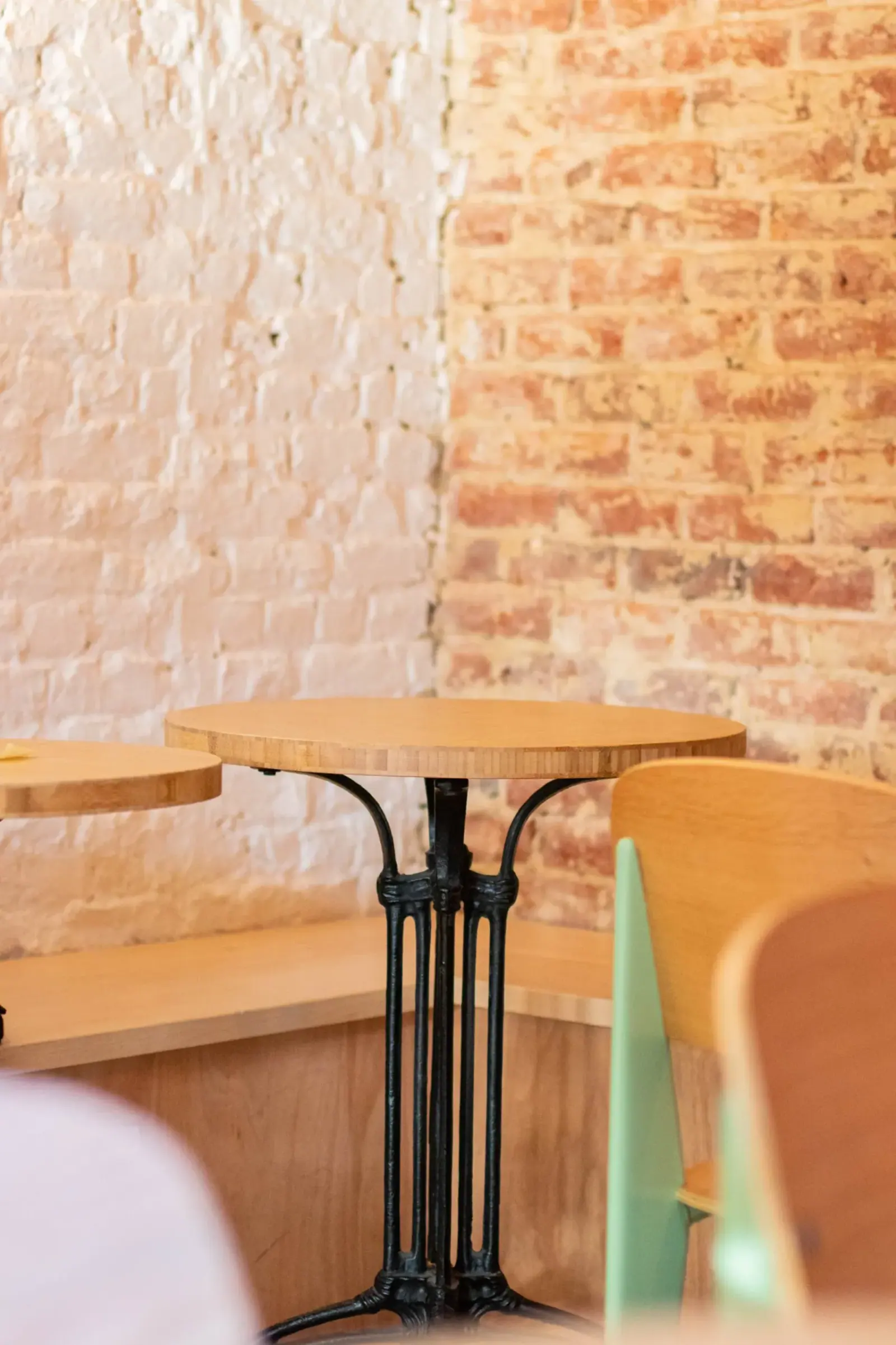 Holy Bagels — petite table et banquette bois devant un mur en briques peintes