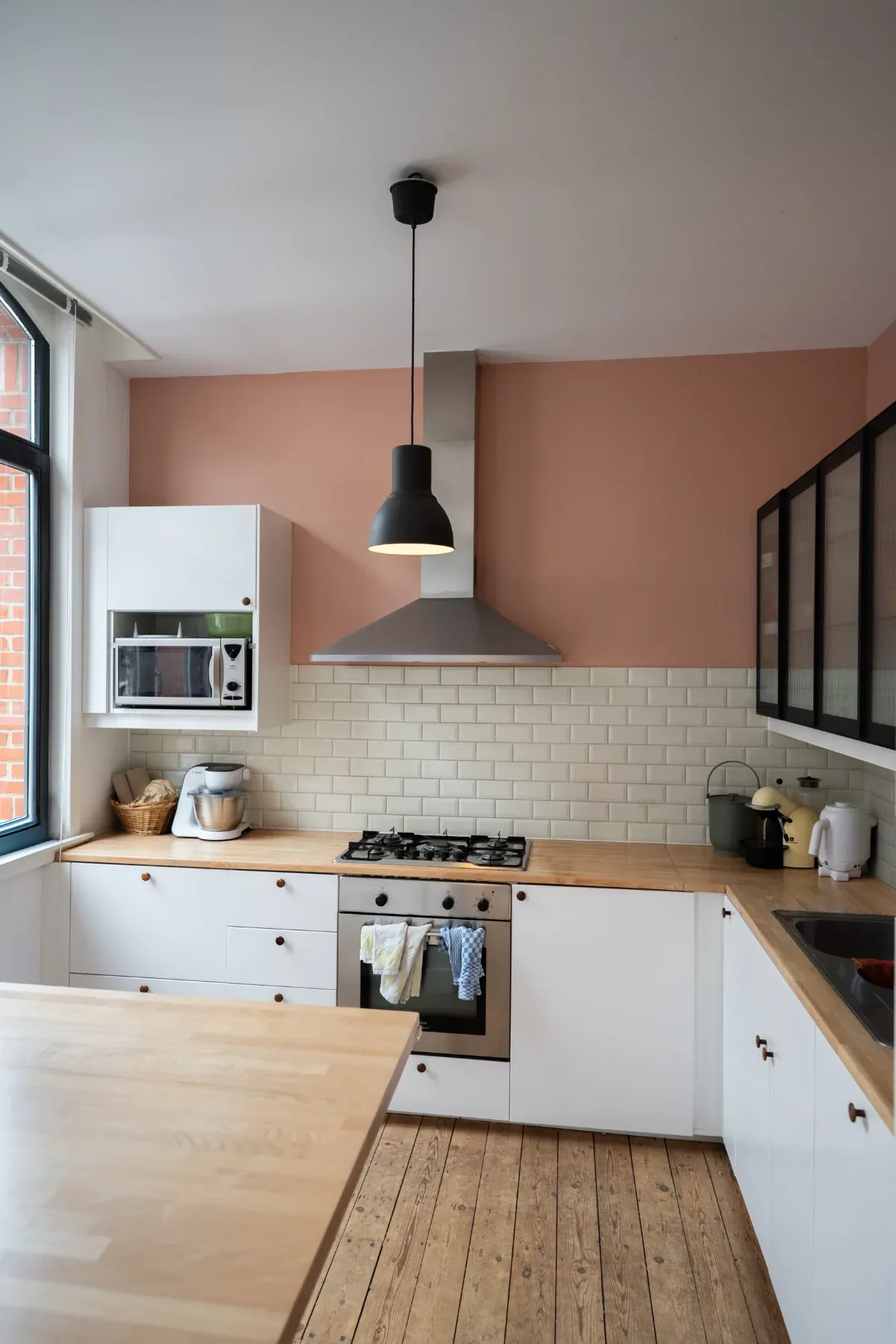 Laeken — cuisine rose, hotte métallique, plan de travail bois et verrière